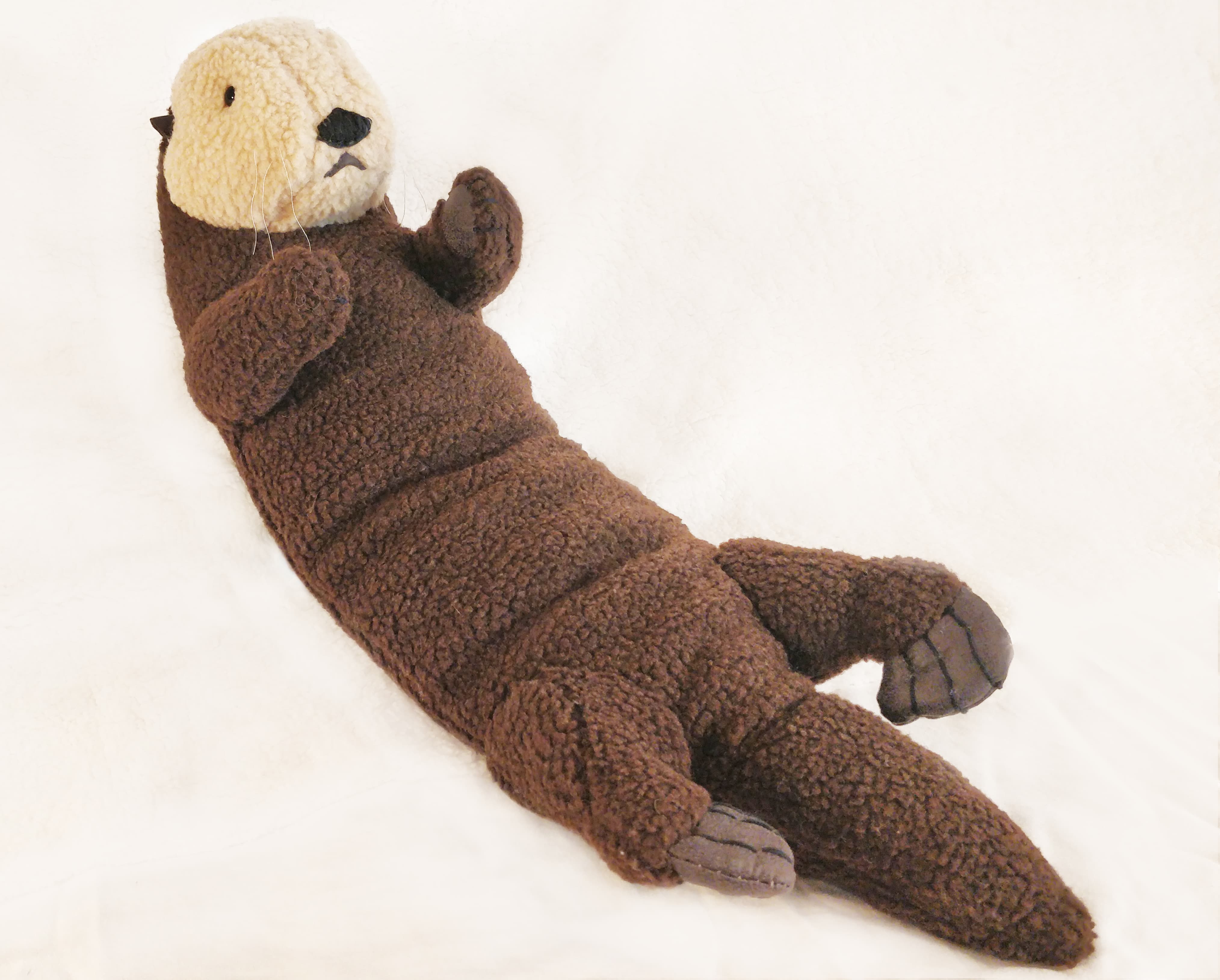 Soft toy otter lying down on a surface, on it's back.