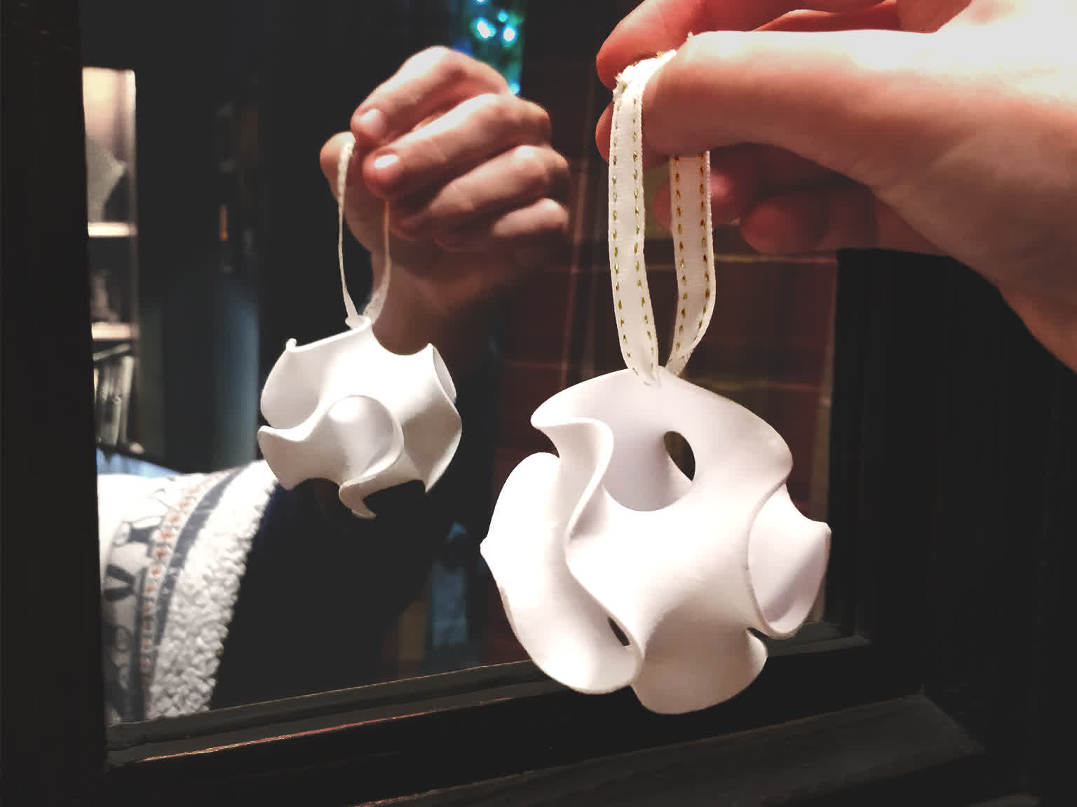 A gyroid christmas ornament, held up to a mirror